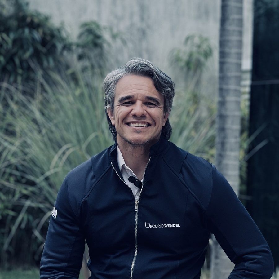 Dr. Rodrigo Wendel sentado no jardim da clínica, sorrindo para a câmera